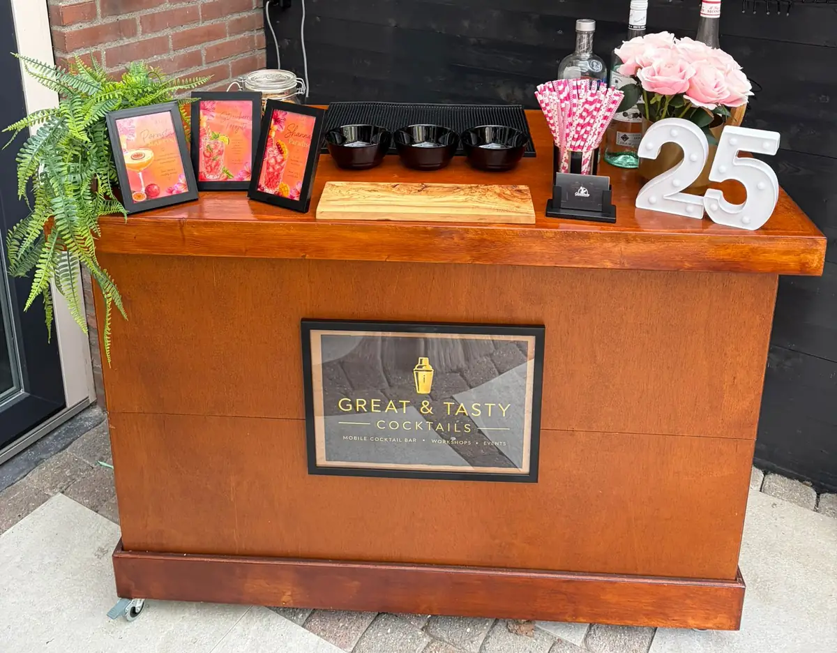 De mobiele bar van Great & Tasty frontaal, met gin op het werkblad, cocktailkaarten in lijstjes en het logo achter glas aan de voorkant