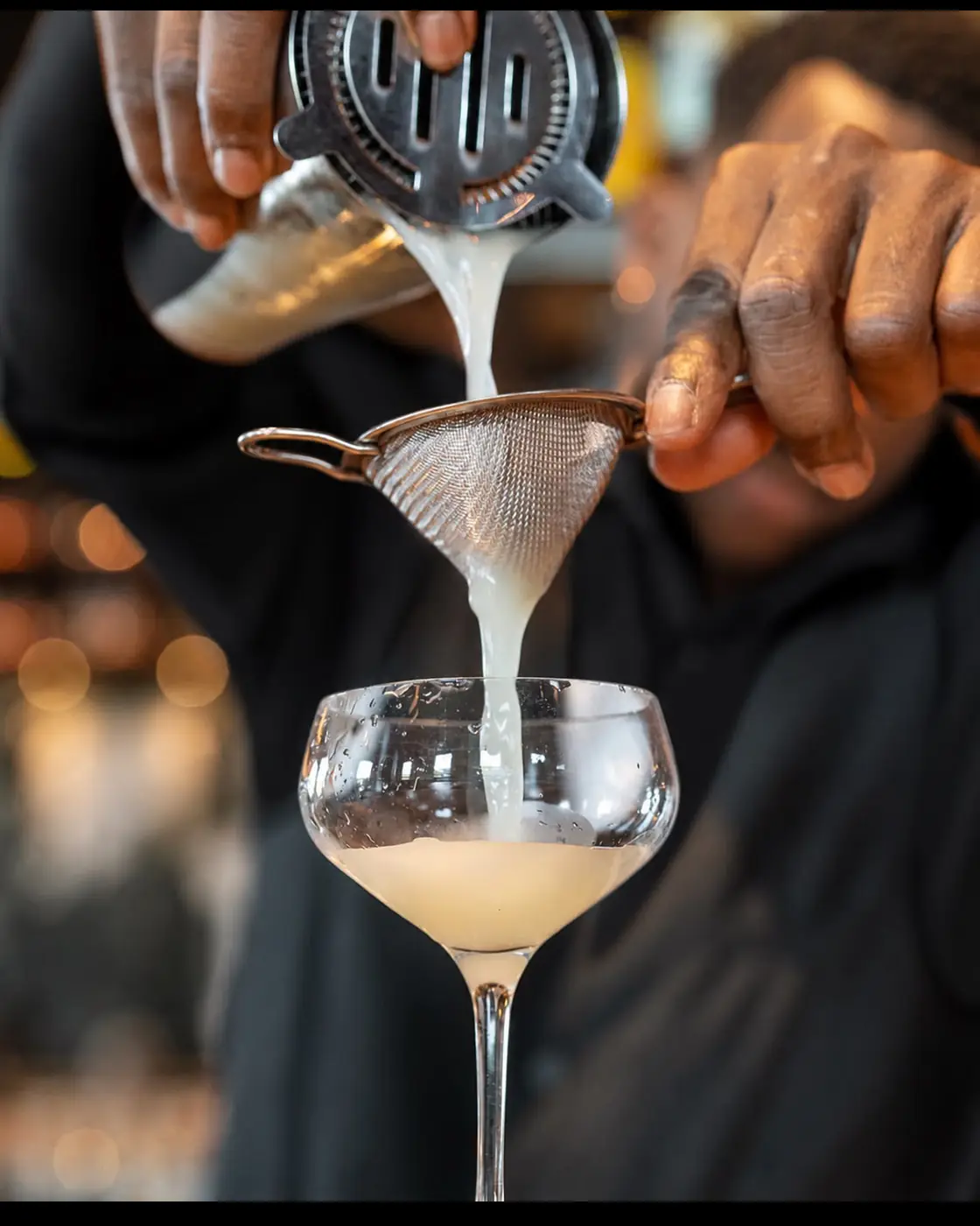 Rudy zeeft een cocktail door een fijne zeef in een coupeglas