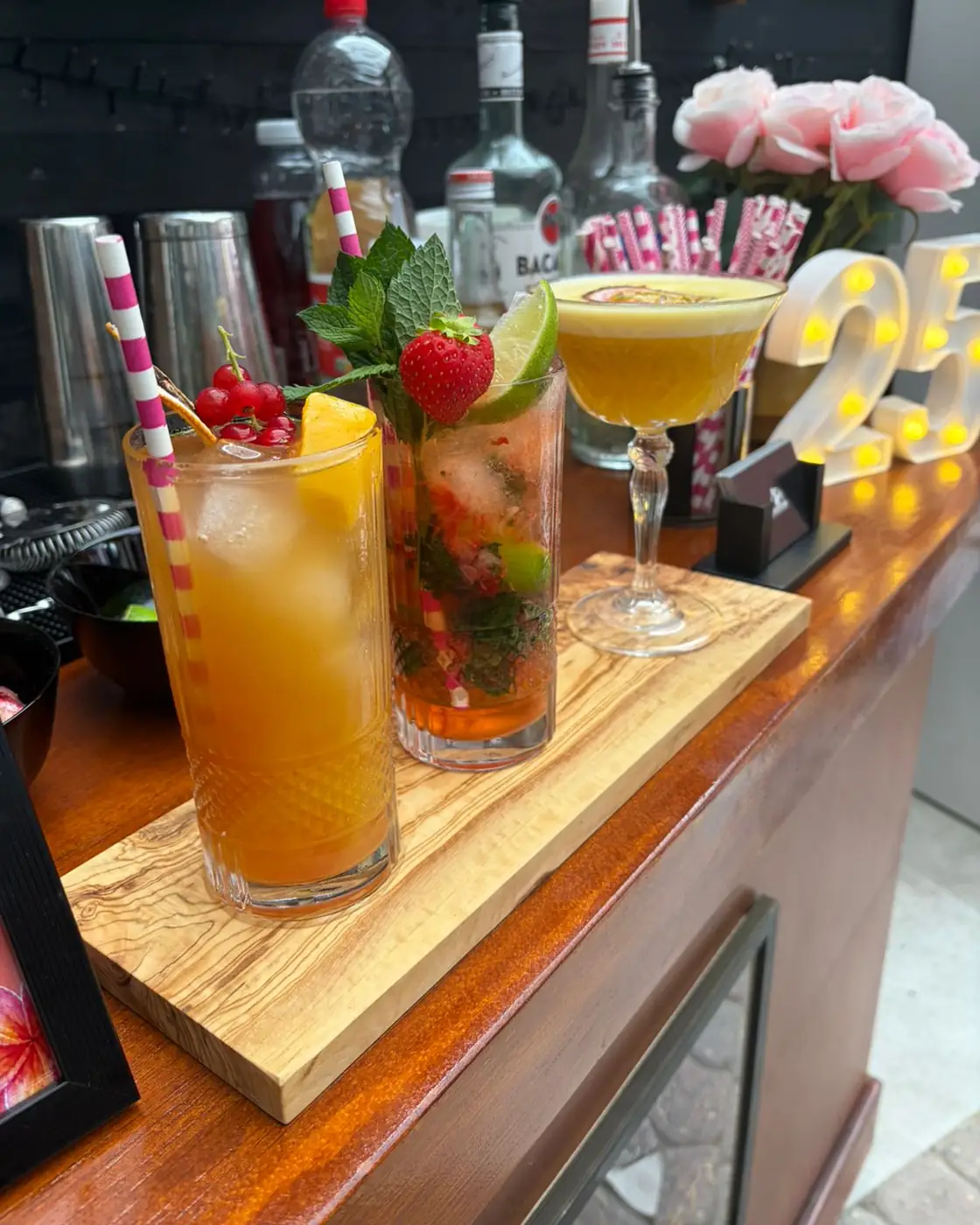 Drie afgemaakte cocktails op een olijfhouten plank op de bar, met verse munt, aardbei en limoen als garnering