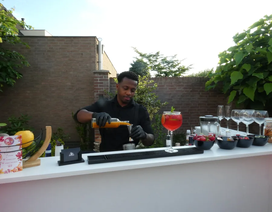 Rudy achter zijn bar in een tuin, met vier gevulde cocktailglazen op de bar