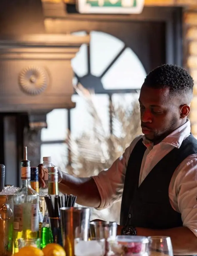 Rudy achter de bar, bezig met het inschenken van een fles